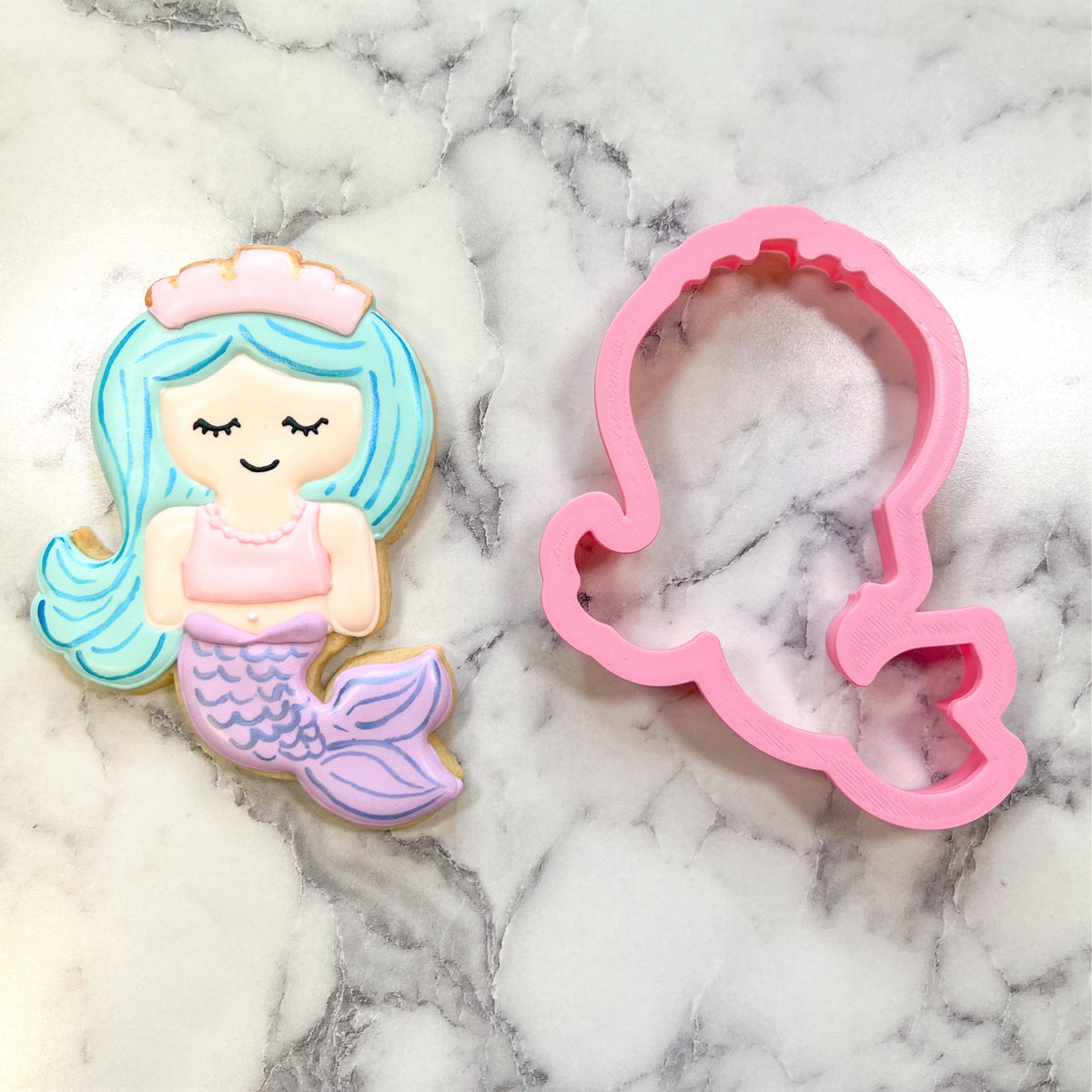 A pink plastic mermaid cookie cutter with detailed head and tail outline from flour box club mermaid with tiara set