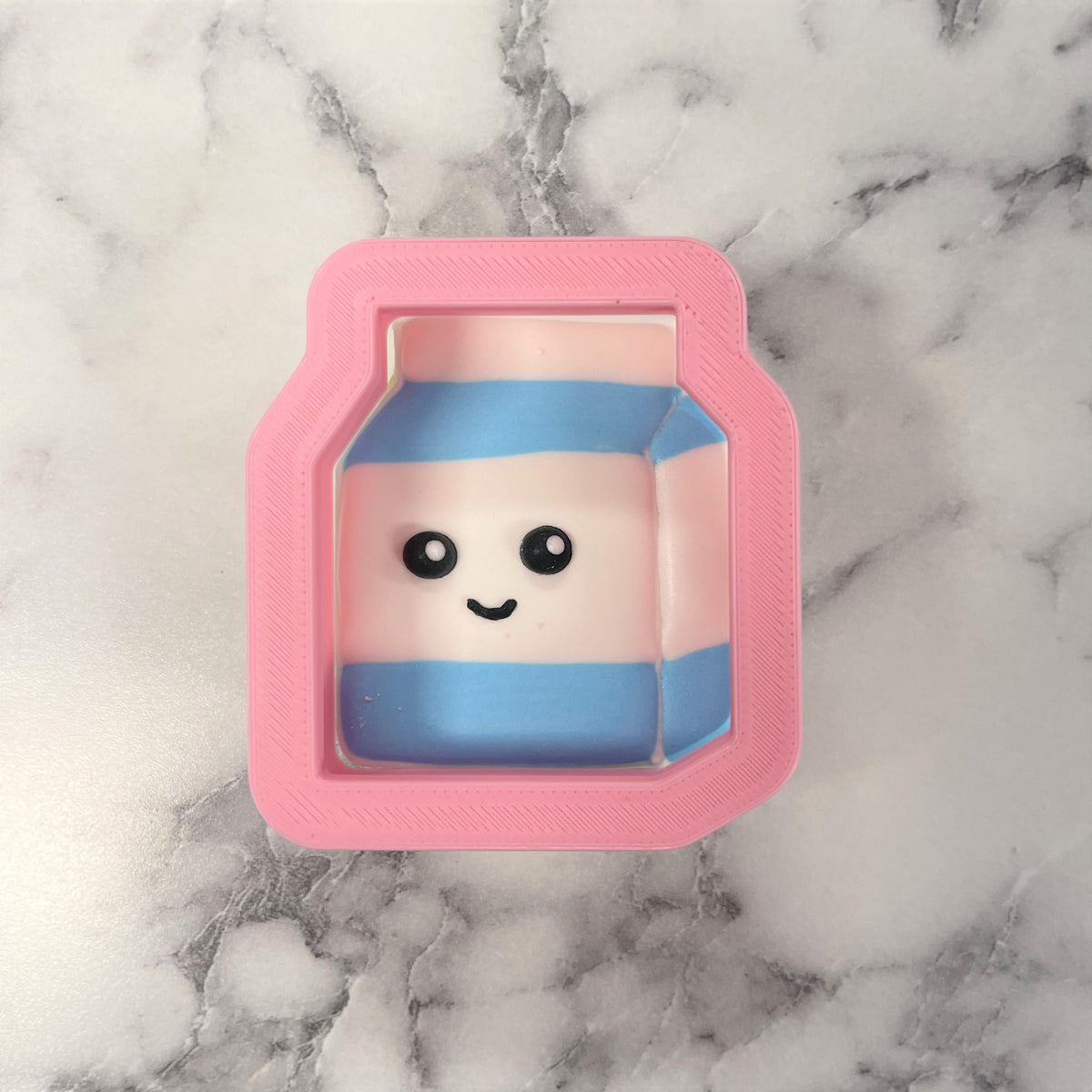 Mini milk box cookie cutter shaped as a pink plastic squishy with blue stripes and a smiling face