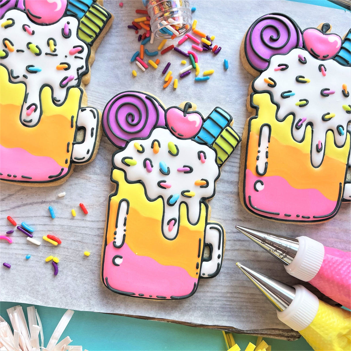 Pastel-colored gradient milkshake cookies decorated with white icing rainbow sprinkles and candy toppings from comic cookie online decorating class recording