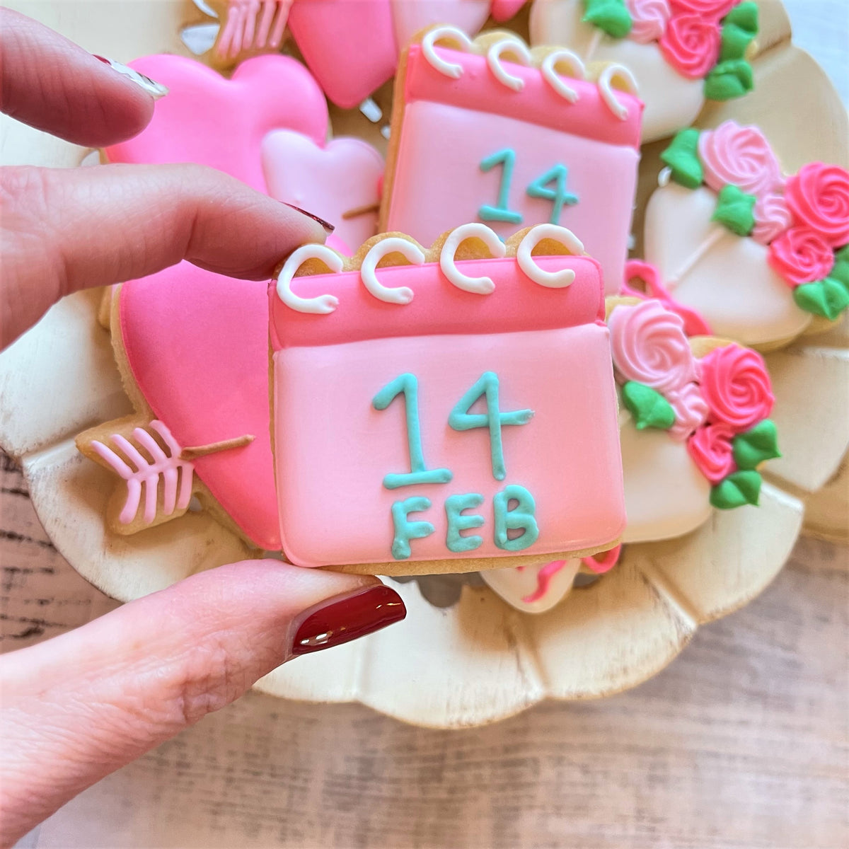 A pink frosted calendar-shaped cookie with 14 feb in teal icing made using a mini calendar cookie cutter