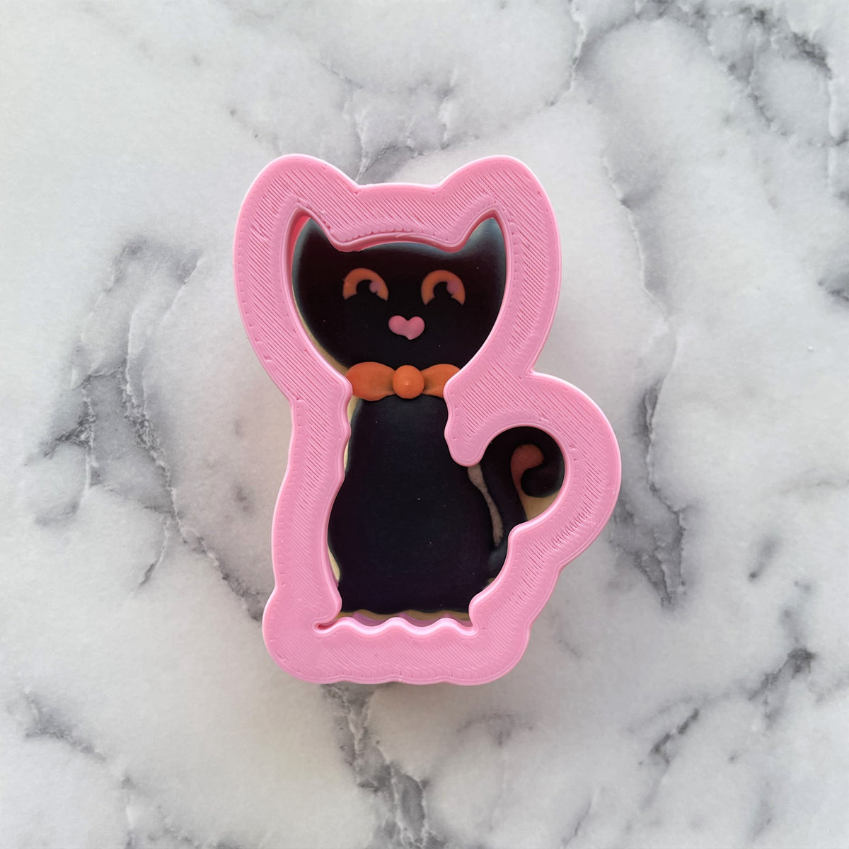 Mini classic black cat cookie cutter made of pink plastic with black interior and orange bow detail for baking