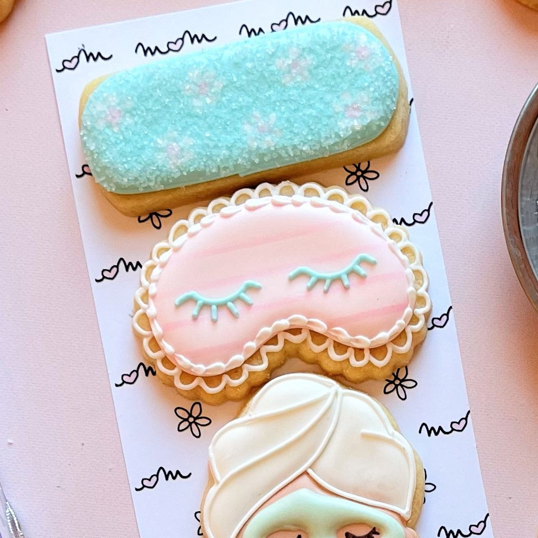 Mini face mask cookie cutter with pastel pink sleep mask cookie decorated with light blue eyelashes and white icing border
