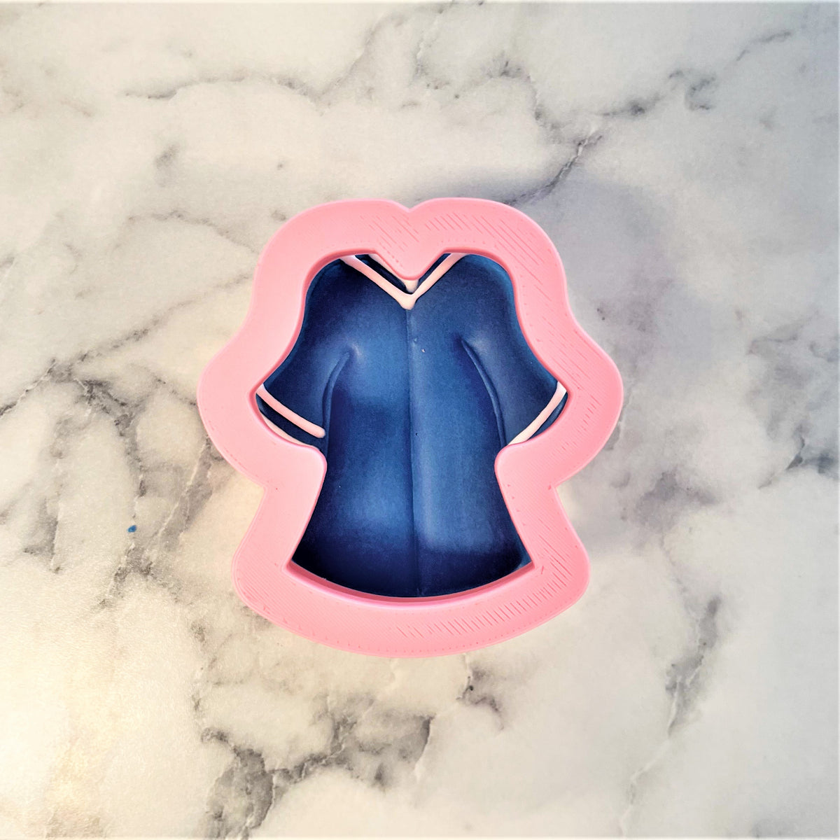 Pink plastic mini grad cookie cutter shaped like a blue nurse uniform with white trim for graduation treats