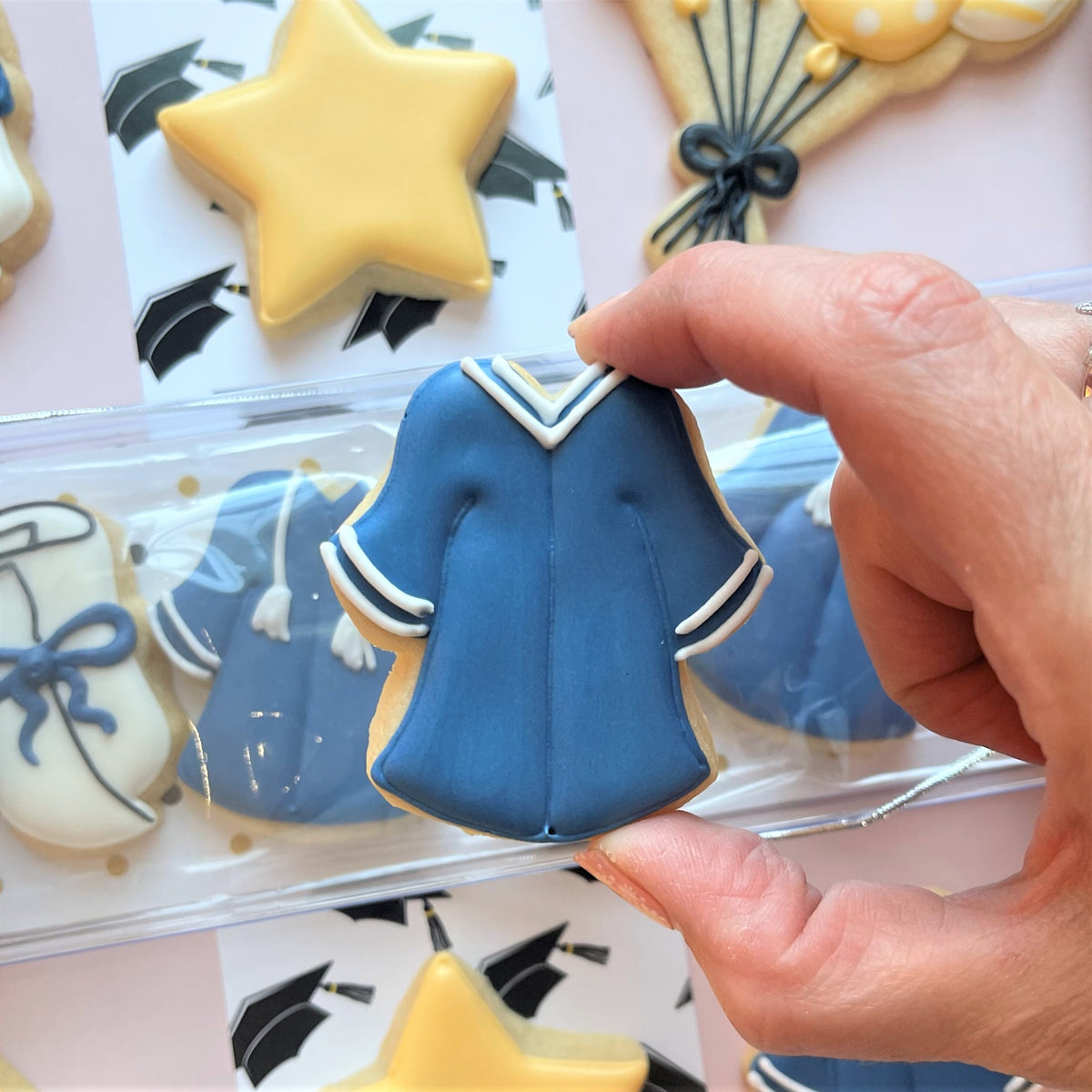 Blue graduation gown cookie with white trim and icing details from mini grad cookie cutter bundle