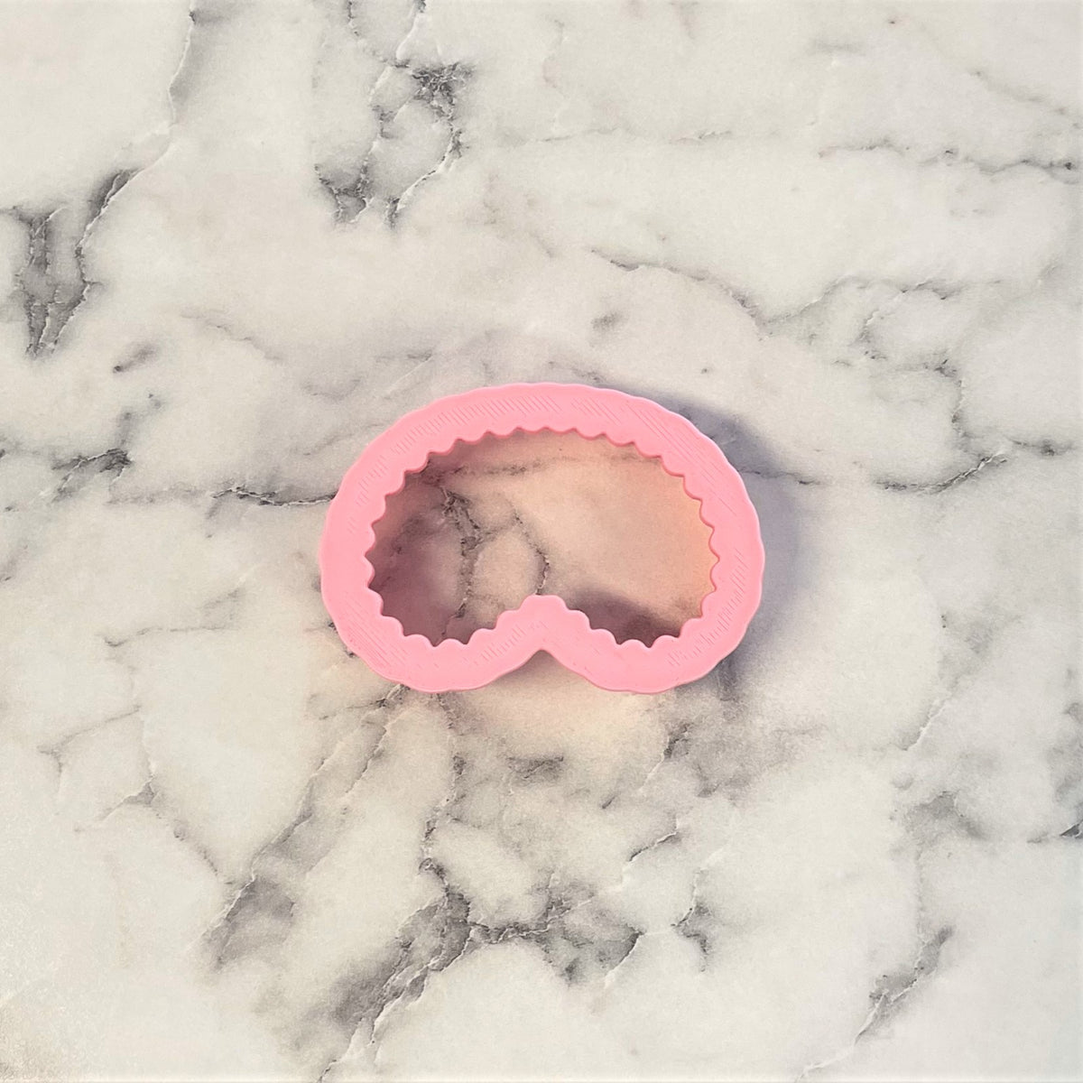 Pink silicone mini face mask cookie cutter mold with scalloped edge design for making sleep mask shaped cookies