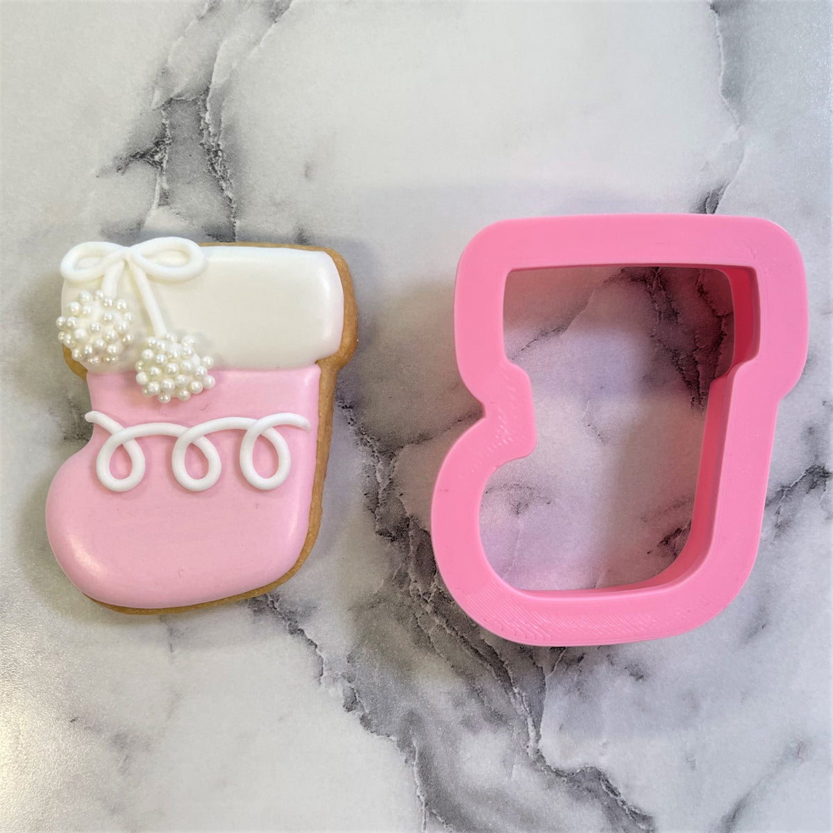 Pink silicone mini classic christmas stocking cookie cutter next to a decorated pink and white sugar cookie shaped like a stocking