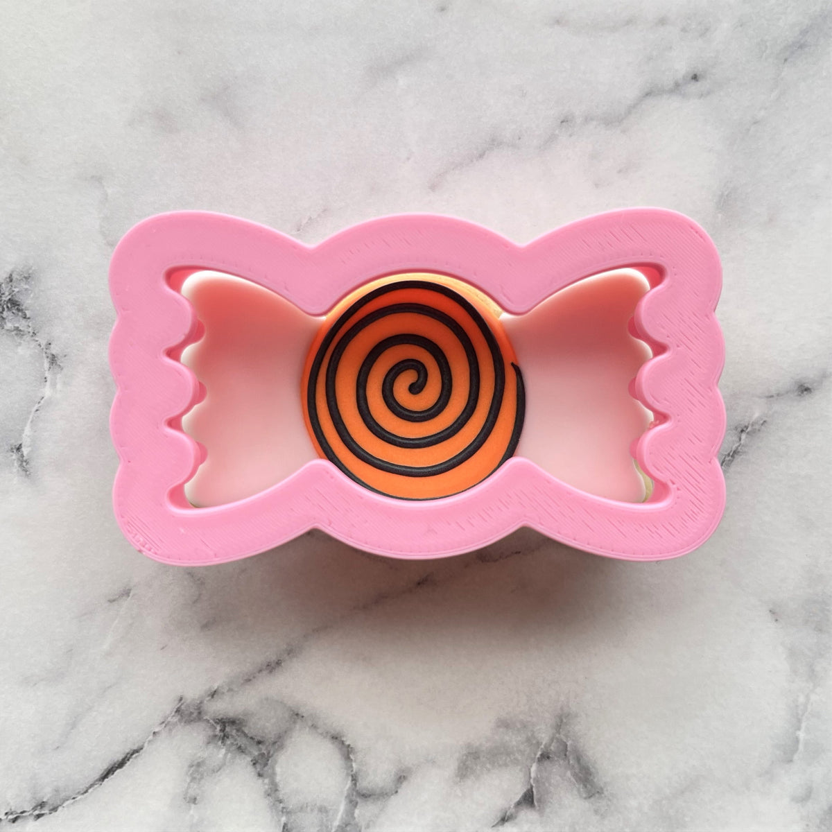 Mini candy wrapped cookie flip cutter in pink with an orange and black spiral design for festive baking
