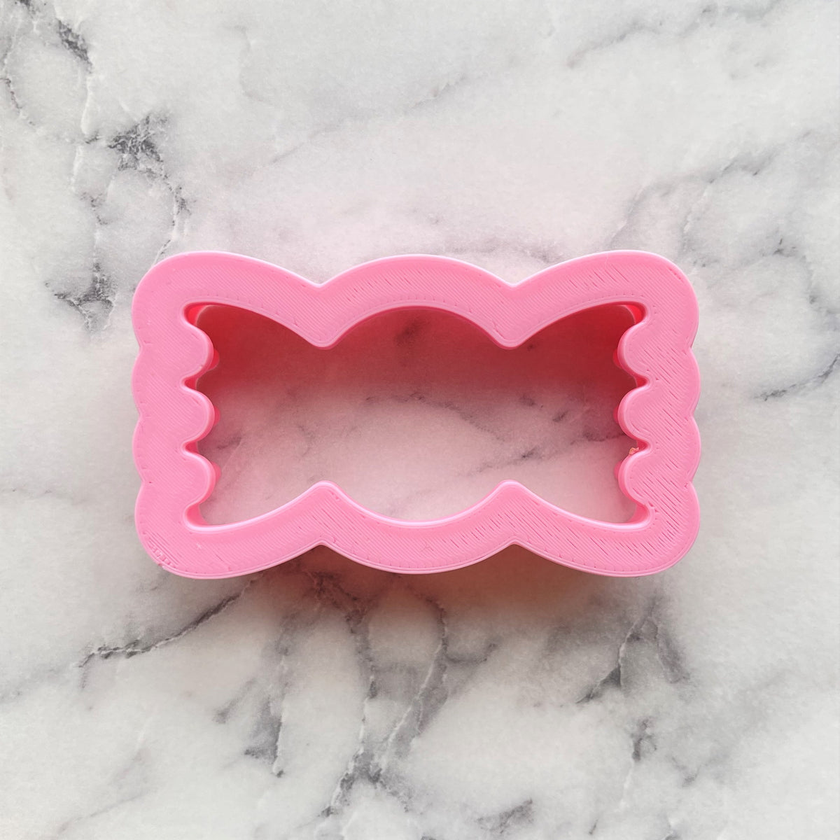 Mini candy wrapped cookie flip cutter is a pink plastic bow-shaped cookie cutter for baking and crafts