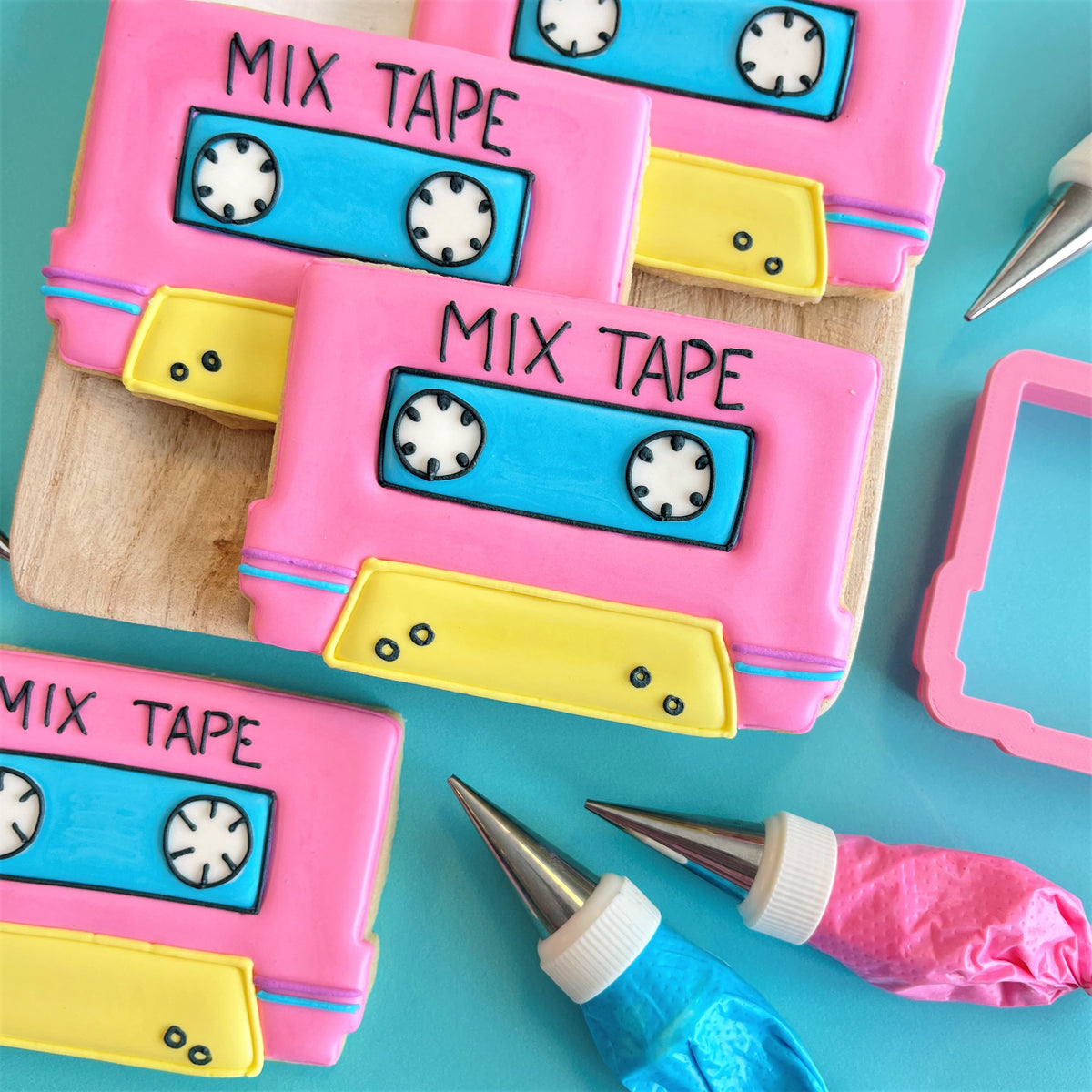 Pink and yellow fondant decorated mix tape cookies with blue cassette labels and black lettering for totally 80s cookie class