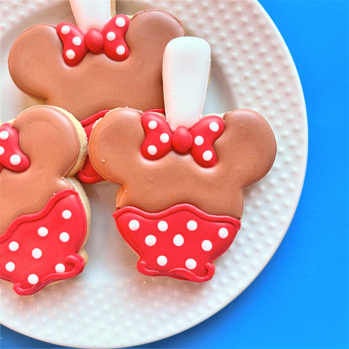 Chocolate-colored Minnie Mouse shaped cookies with red polka dot bows and skirts for mouse snacks online cookie decorating class recording