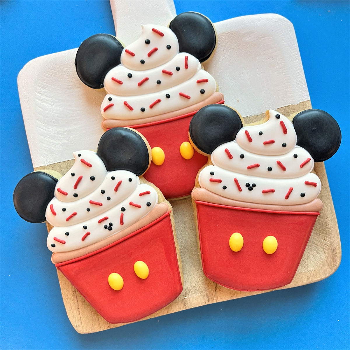Three mickey mouse-themed cupcake cookies with red base yellow buttons and white icing swirls from mouse snacks class recording