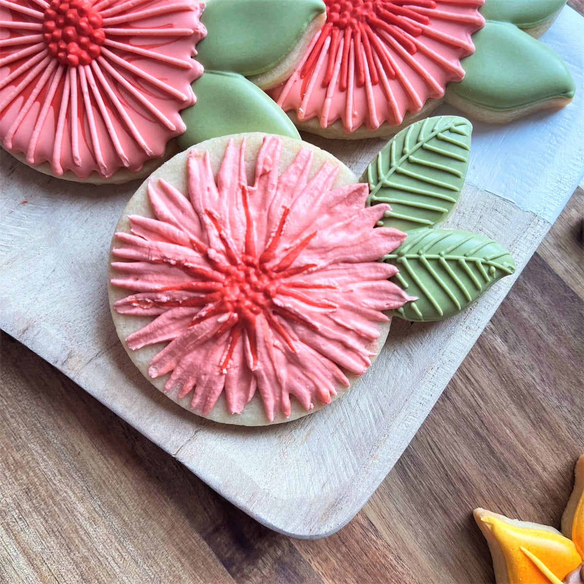 Pink and red flower shaped sugar cookies with green leaf icing made using mum cookie cutter for decorative baking