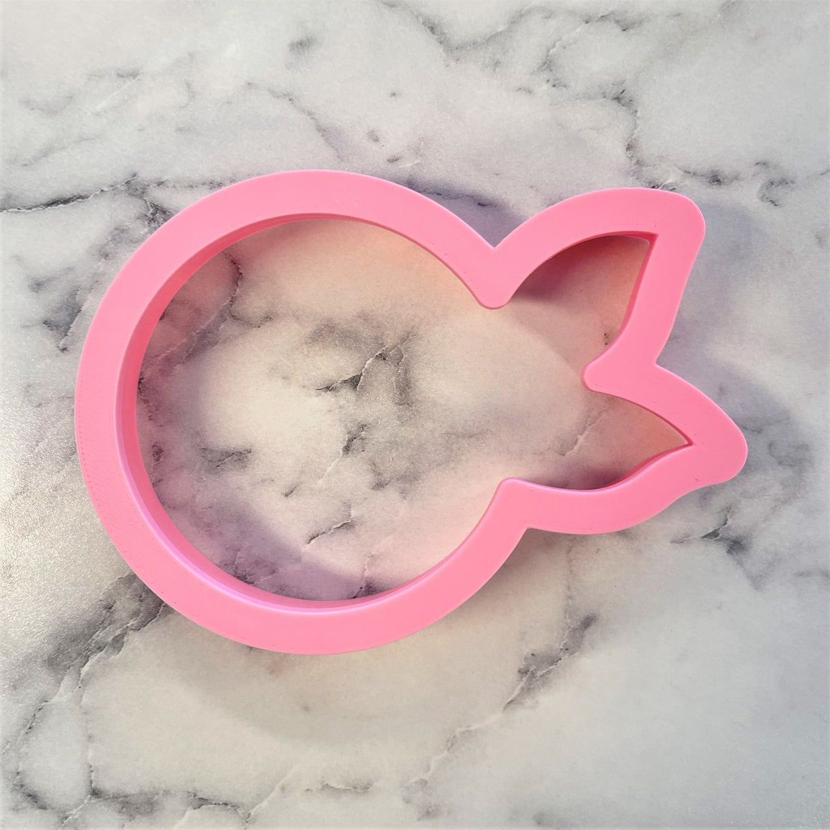 Pink silicone mum cookie cutter shaped like a fish with a smooth glossy finish and clear interior showing marbled pattern