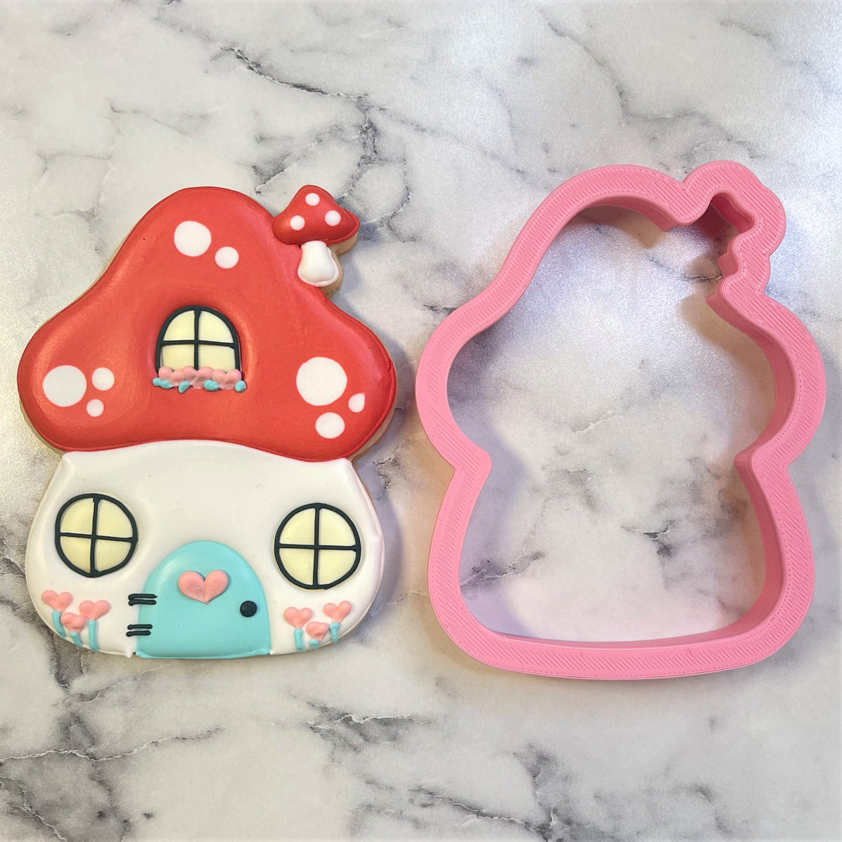 A whimsical red and white mushroom house cookie with turquoise door pink hearts and tiny windows made with a cutter