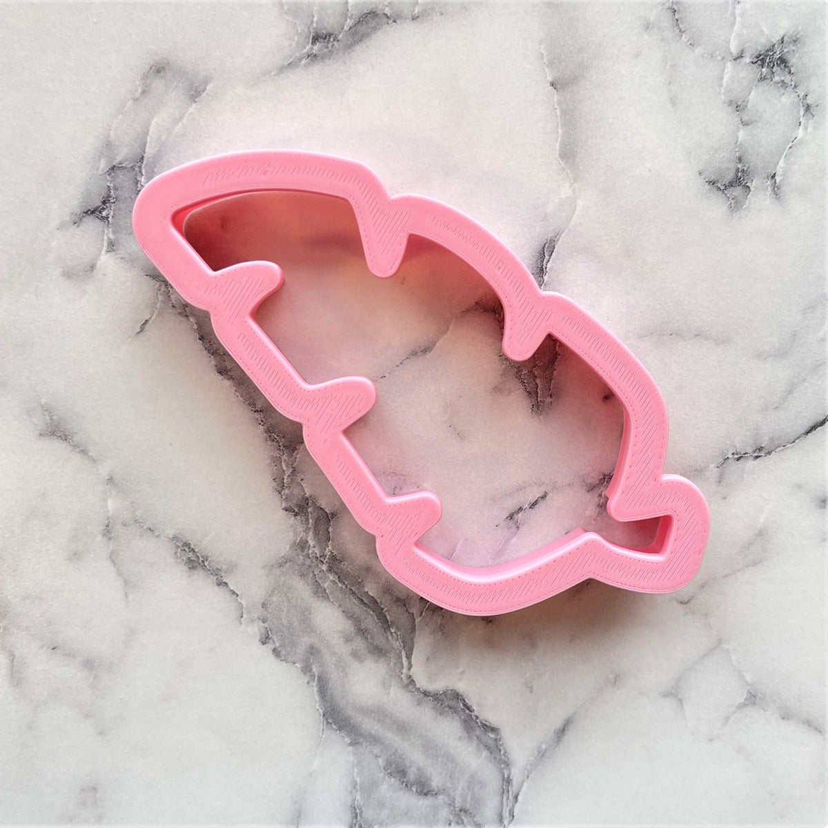 Pink plastic palm branch cookie cutter shaped like a feather for baking and crafting purposes