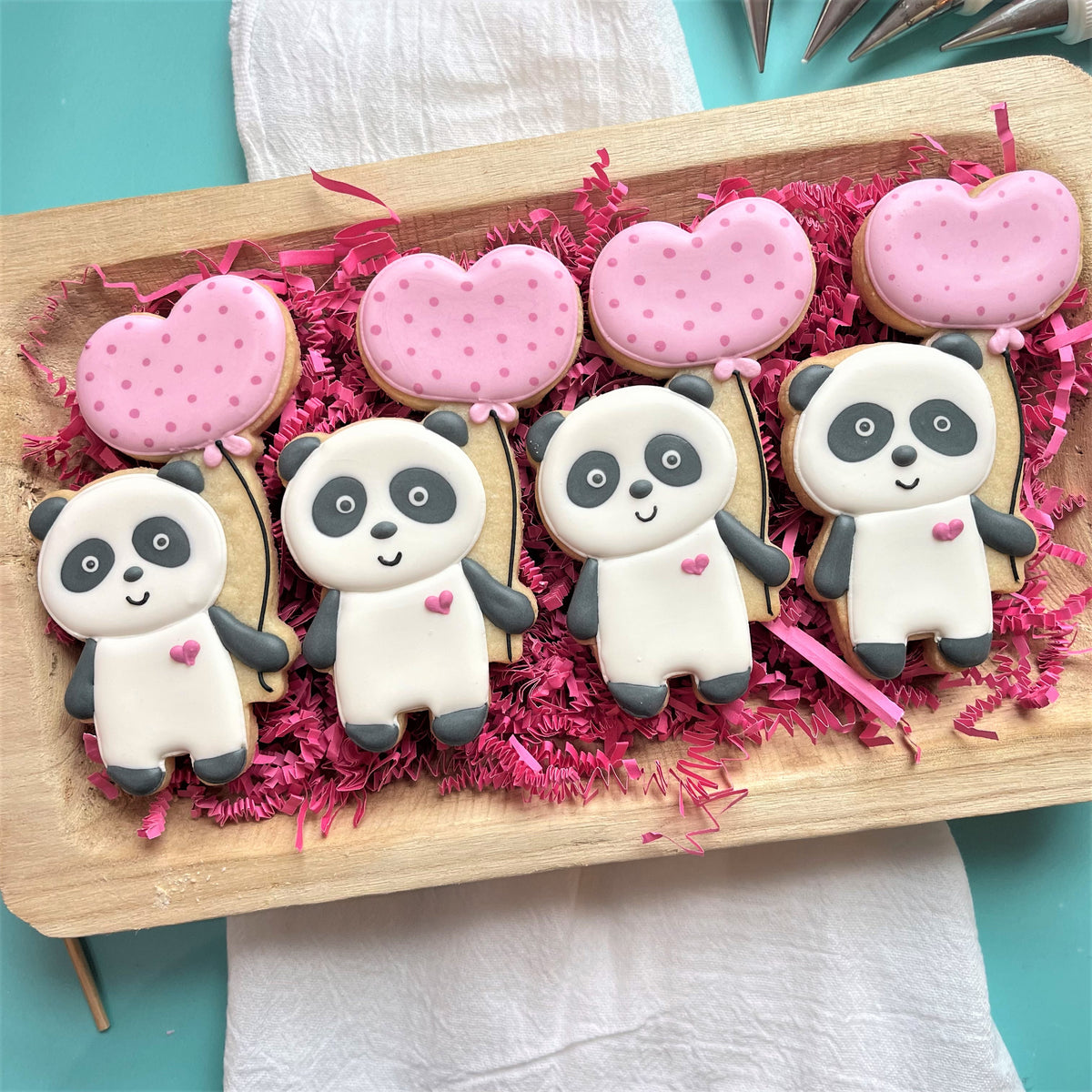 Cute white and black panda-shaped sugar cookies with pink polka-dotted heart balloons decorated with fondant icing