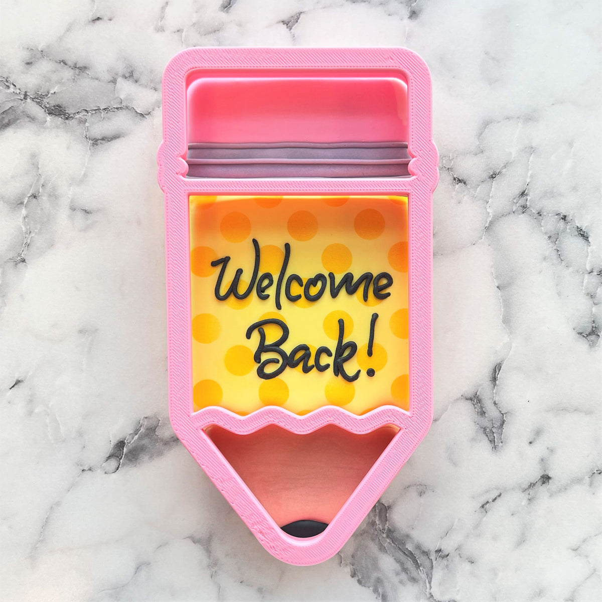 Pink pencil-shaped 3-in-1 multi-cookie cutter with yellow polka-dot interior and welcome back text in black script