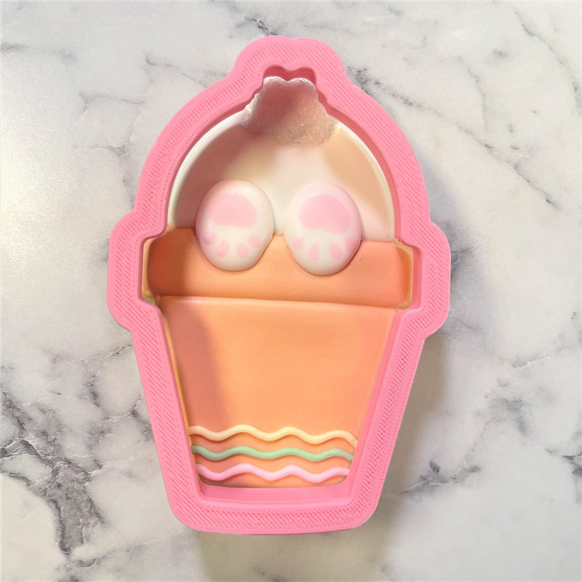 Potted bunny butt cookie cutter in pink silicone with peach base white whipped cream top and pastel wavy stripes