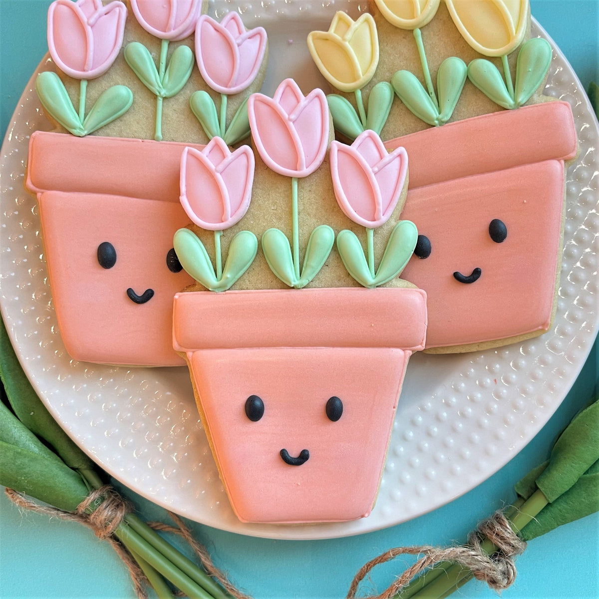 Pink sugar cookies shaped like smiling flower pots with pink and yellow tulip icing made using potted tulips cookie cutter