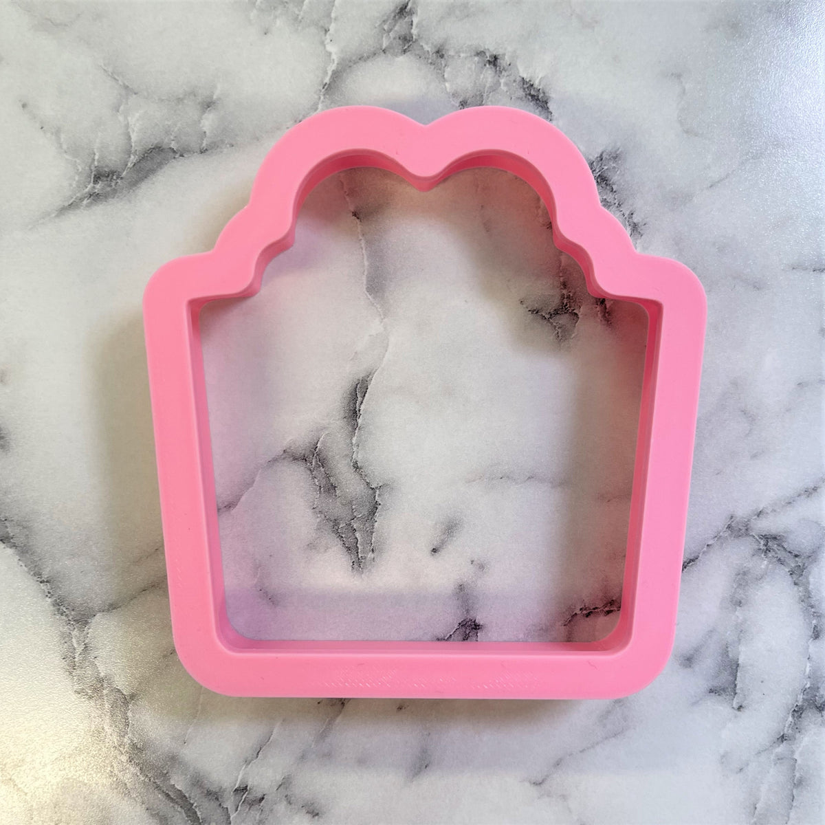 Pink silicone cookie cutter shaped like a gift box with scalloped edges for classic present baking designs