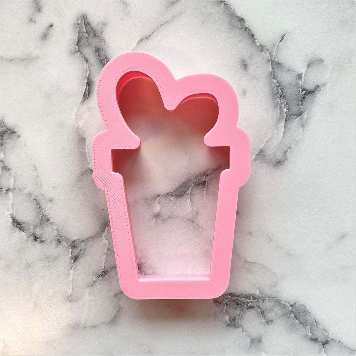 Pink silicone small cookie cutter shaped like a cup with two heart-shaped handles present with bow design