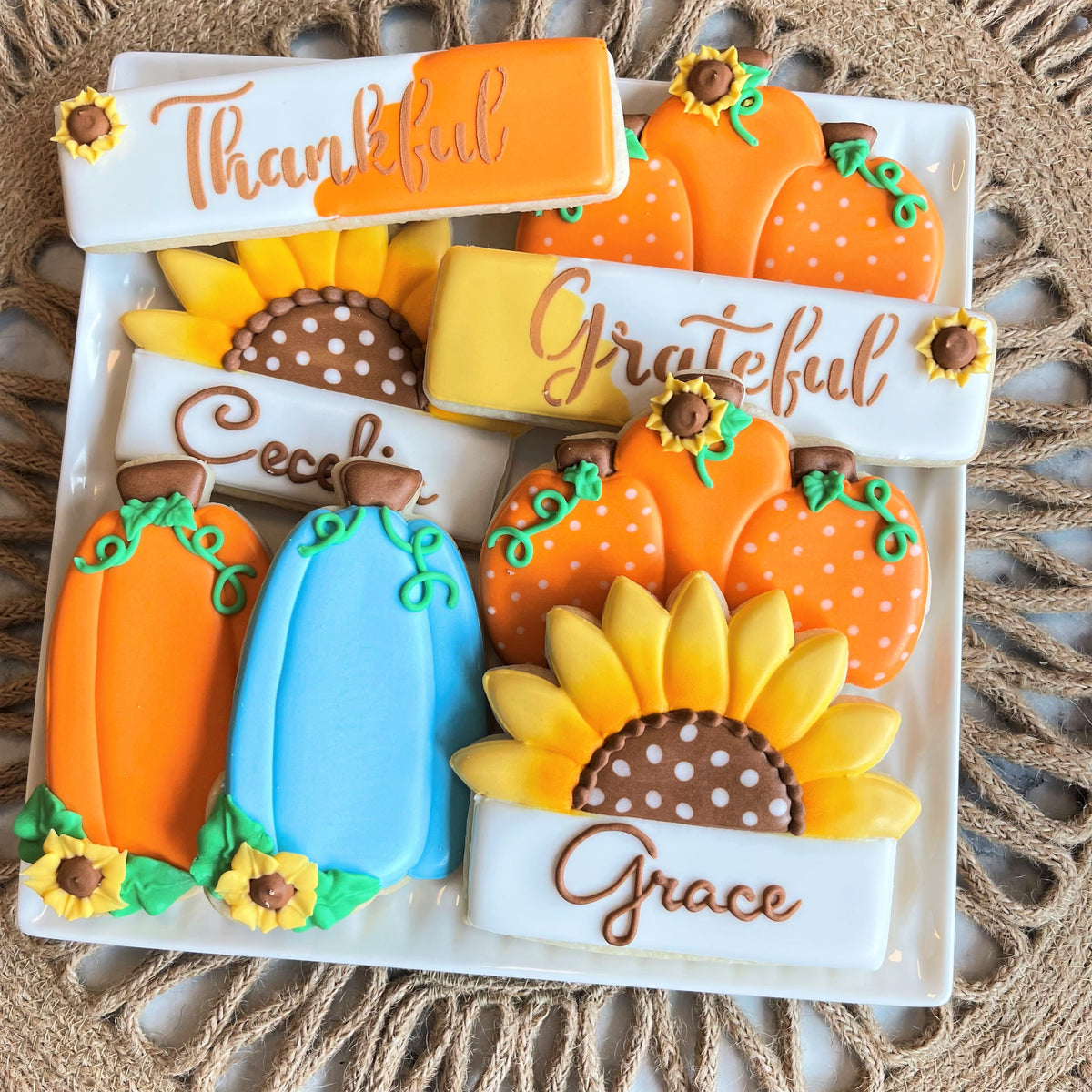A collection of autumn-themed sugar cookies with orange and blue pumpkins sunflowers and thankful grateful inscriptions using pumpkin tall with sunflower cookie cutter