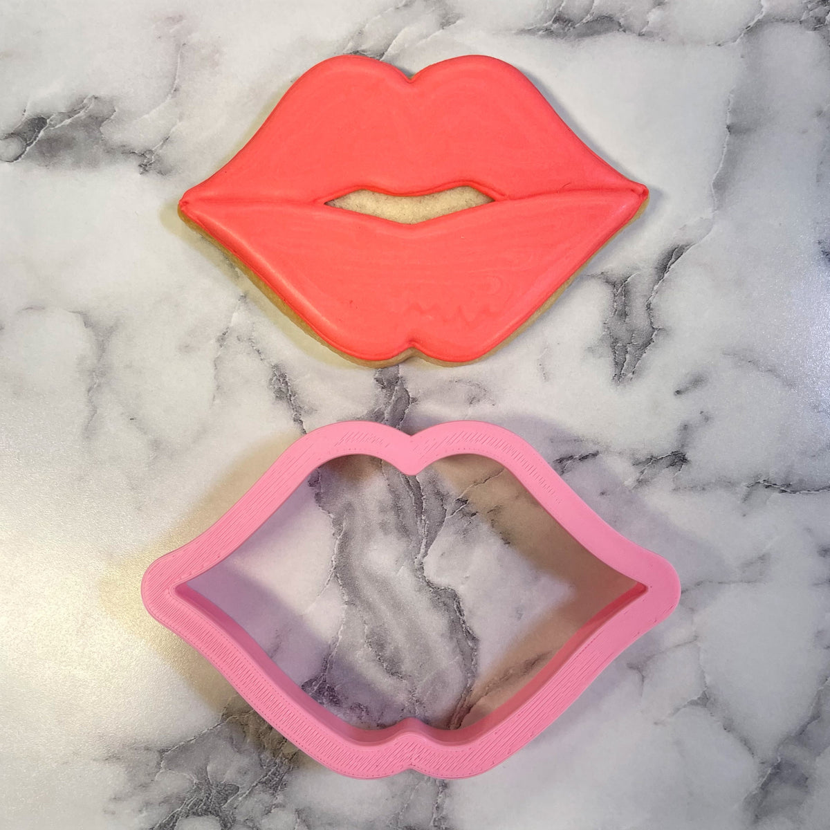 A vibrant coral-pink puckered lips cookie with glossy icing and a small bite taken out of the center
