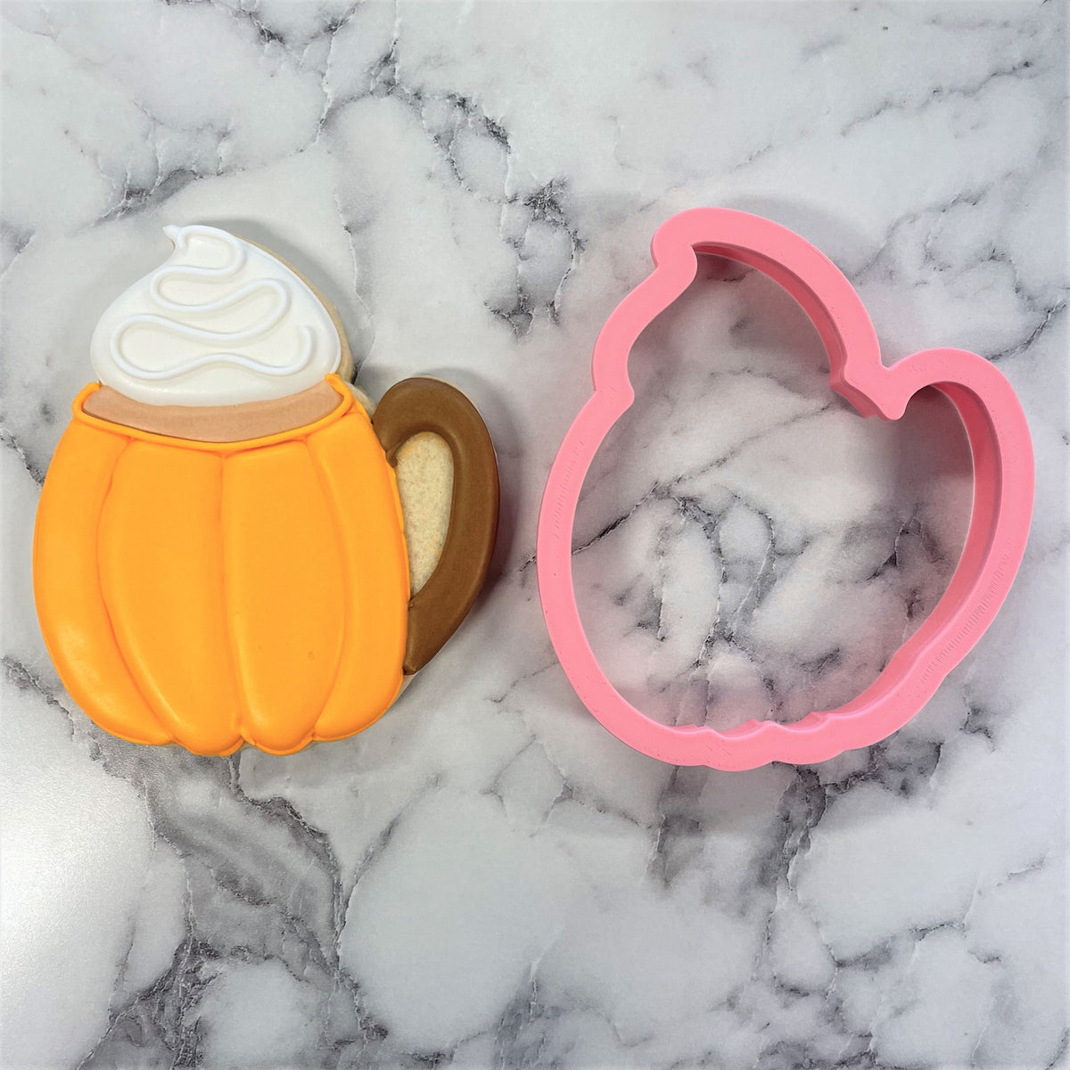 Orange pumpkin latte cookie cutter with brown handle and white icing swirl next to pink silicone mold