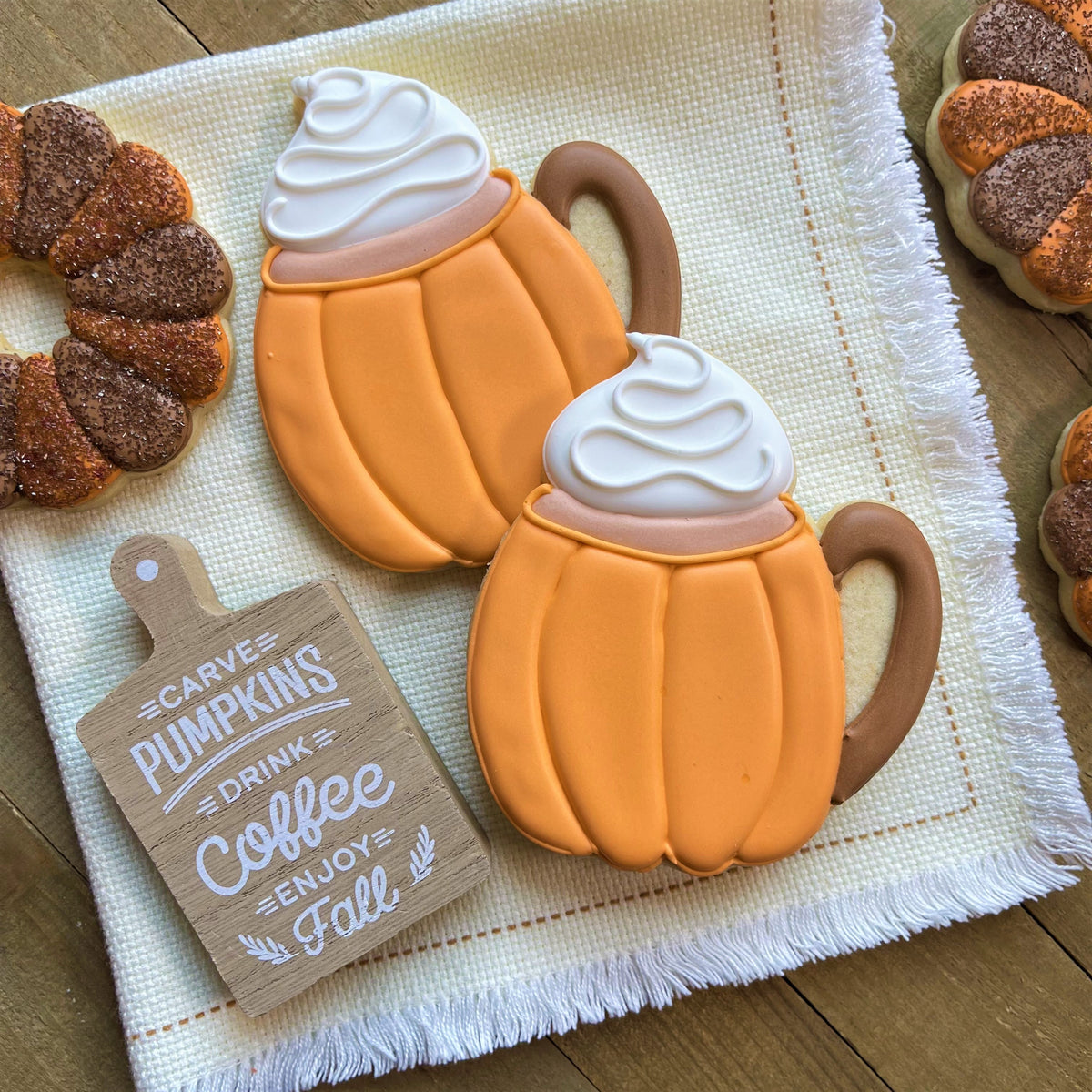 Two orange pumpkin-shaped cookies with white frosting swirls resembling coffee mugs made with pumpkin latte cookie cutter