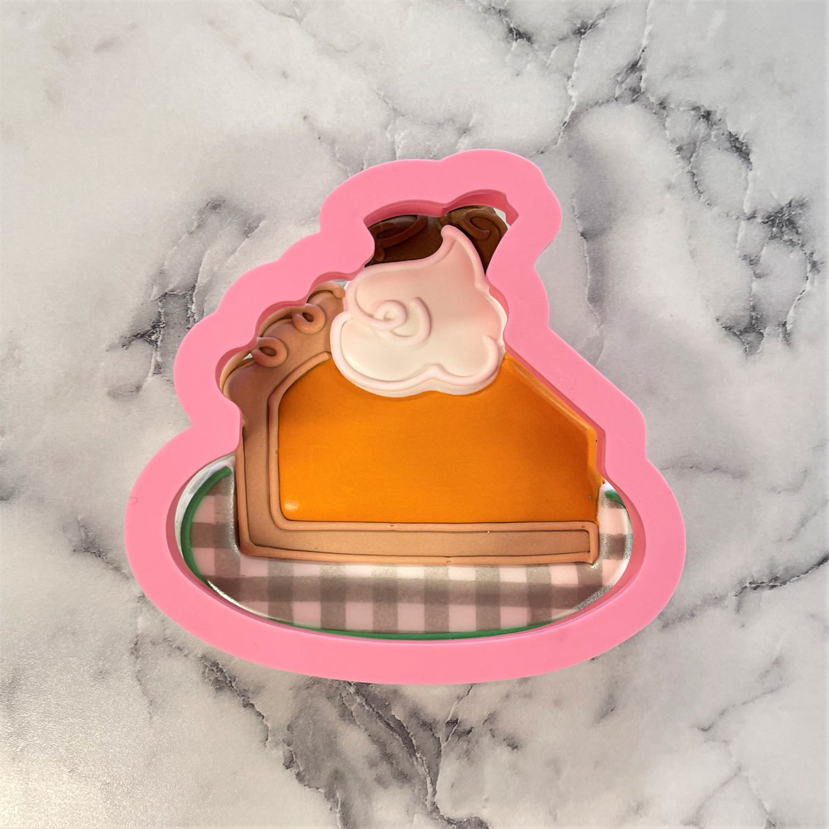 Pink silicone cookie cutter shaped like a pumpkin pie slice with orange filling brown crust and white whipped cream topping