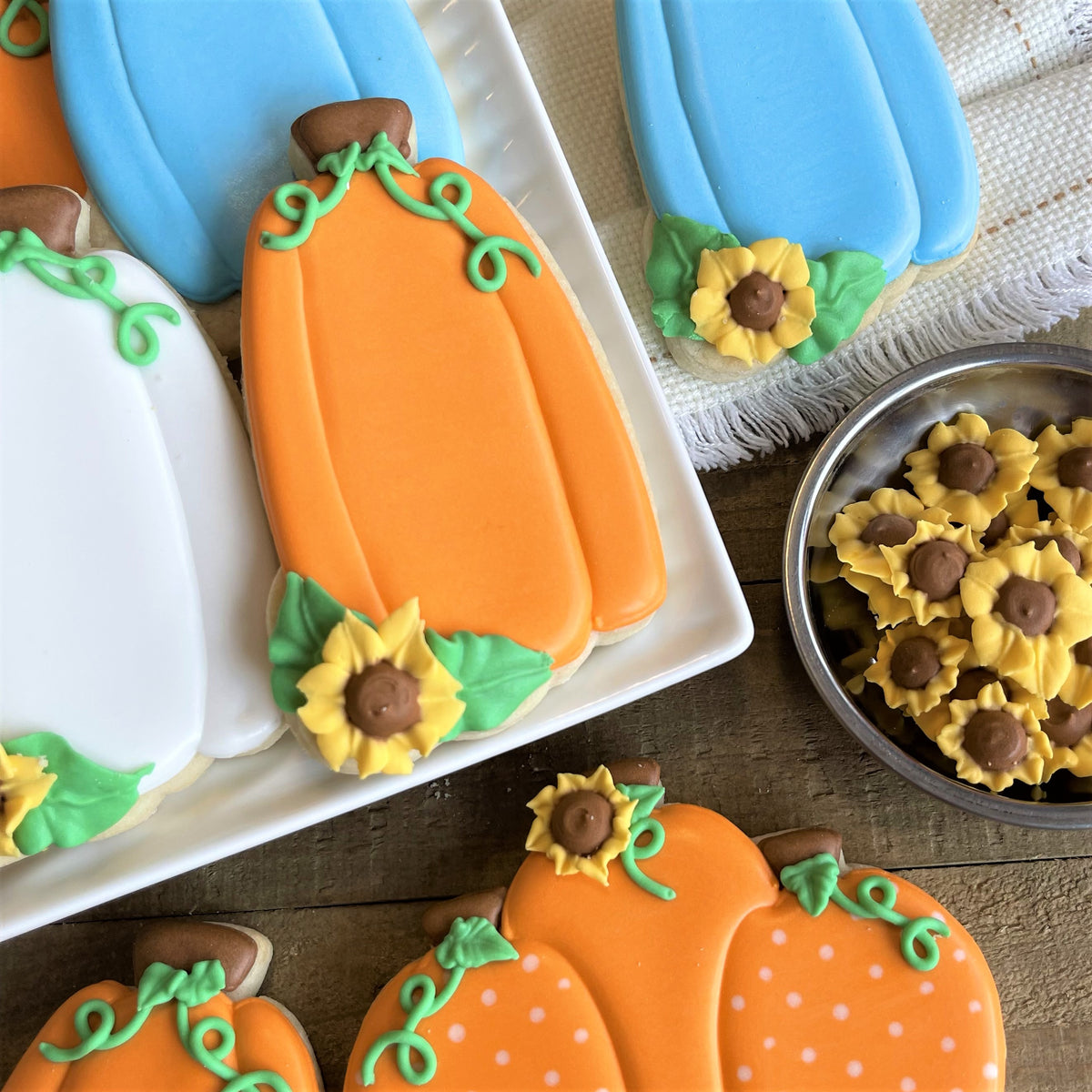 Orange pumpkin-shaped sugar cookies with green icing vines and yellow sunflower decorations made with pumpkin tall sunflower cookie cutter