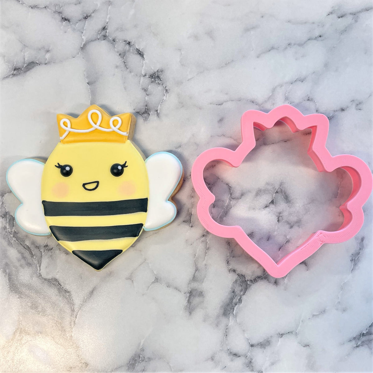 A charming yellow and black queen bee cookie shaped with a gold crown and white wings using the queen bee cookie cutter