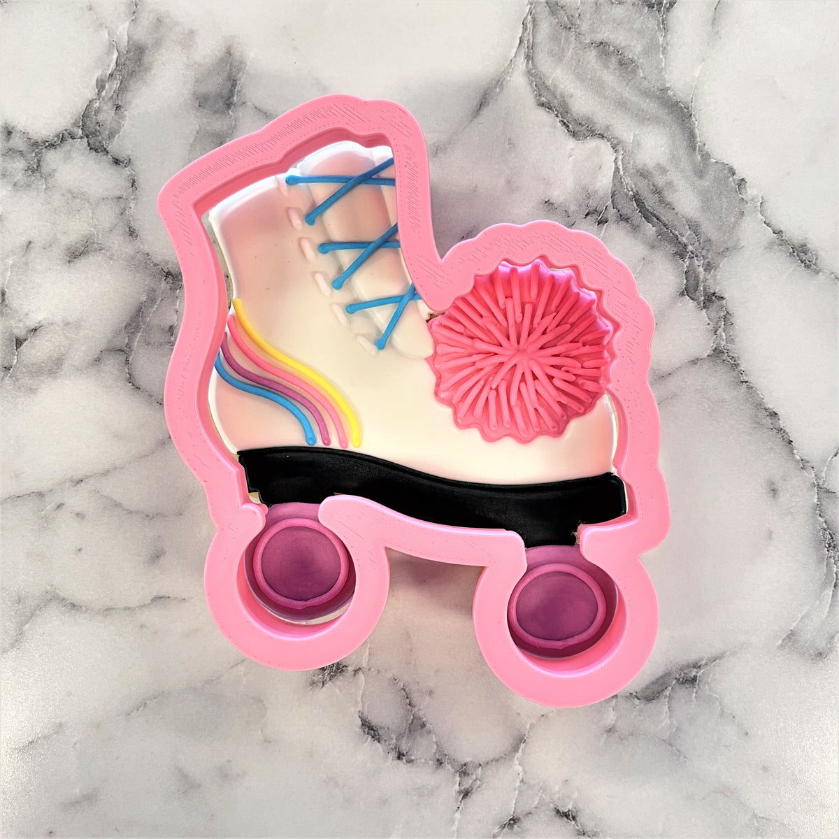 Pink roller skate cookie cutter with white shoe design, rainbow laces, and pink pom pom accent for baking