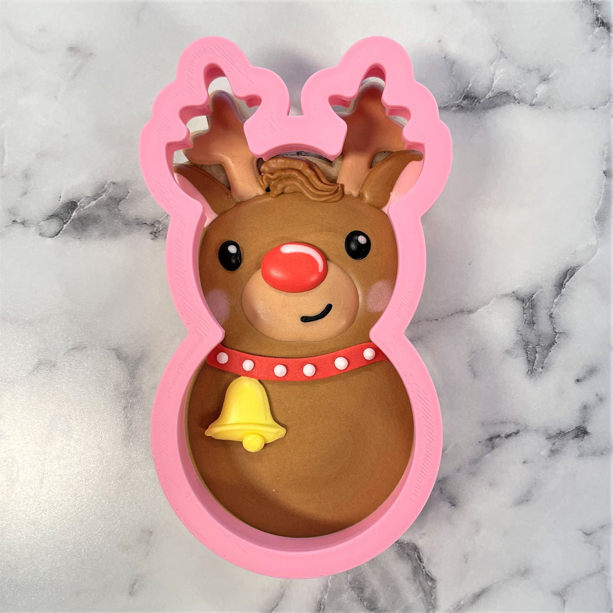 Pink silicone reindeer roly poly cookie cutter with brown details red nose red collar white dots and yellow bell