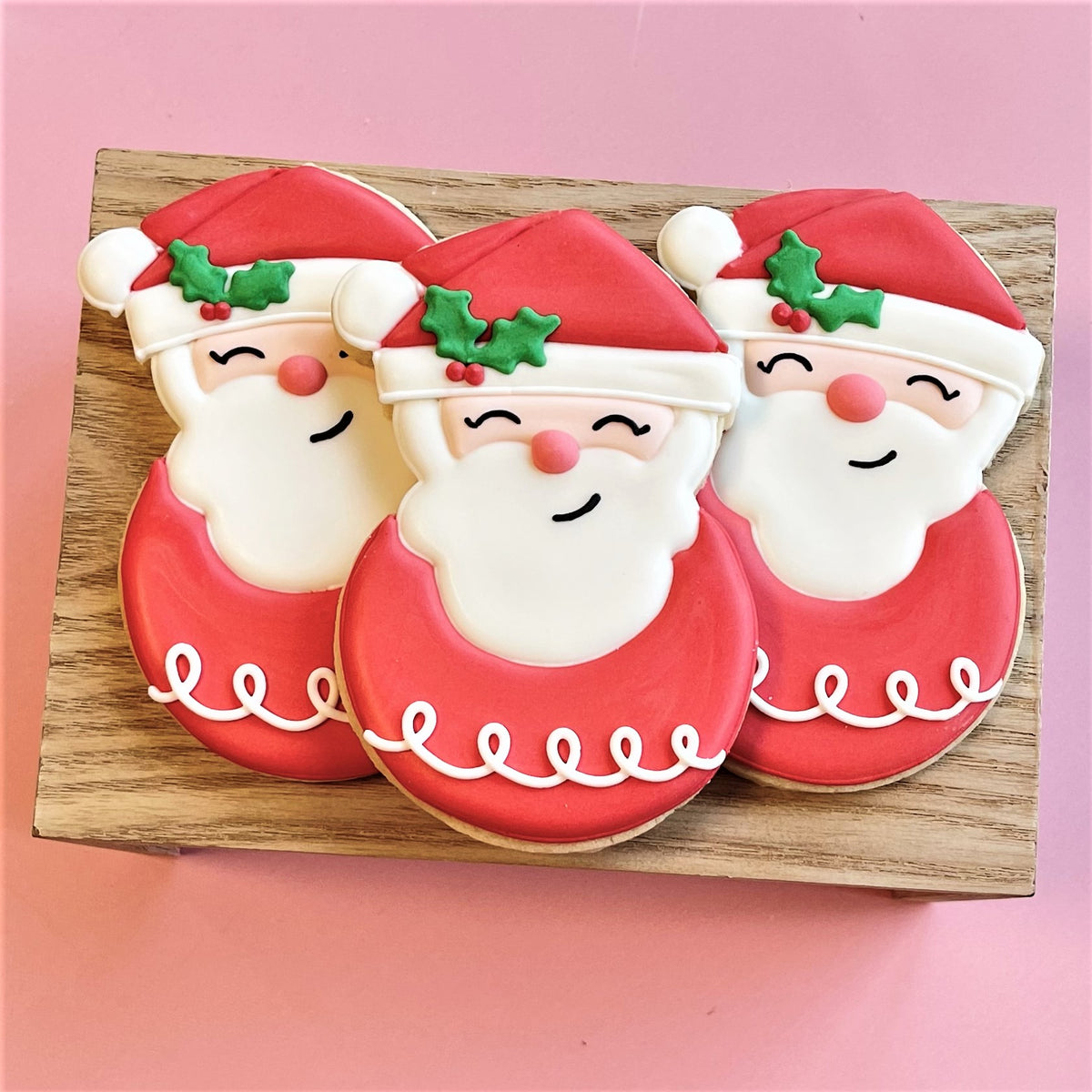 Three festive red and white santa claus cookies with green holly and smiles for holly jolly cookie decorating class recording
