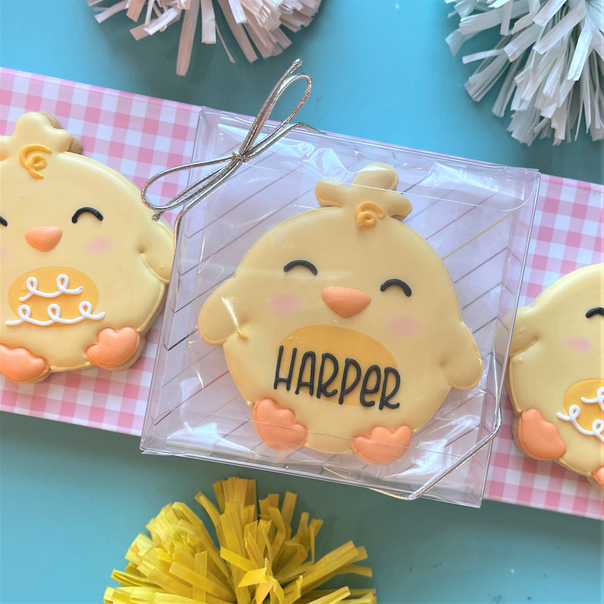 A yellow chick-shaped cookie with orange beak and feet and name harper made using round chick cookie cutter