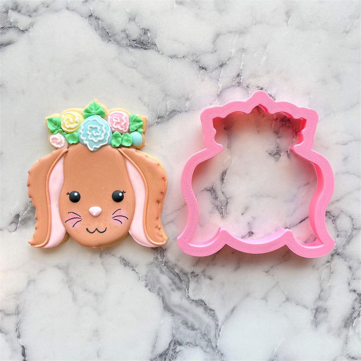 Pink bunny-shaped floral cookie cutter next to a decorated sugar cookie with pastel icing flowers and long ears