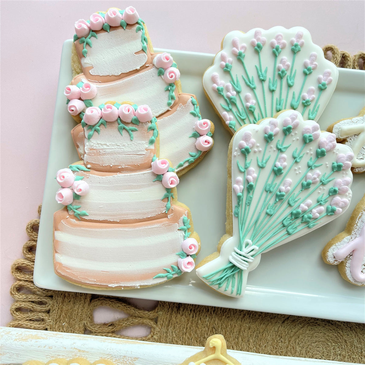 Delicate pastel sugar cookies shaped like a multi-tiered wedding cake and lavender bouquets using wedding bouquet cookie cutter