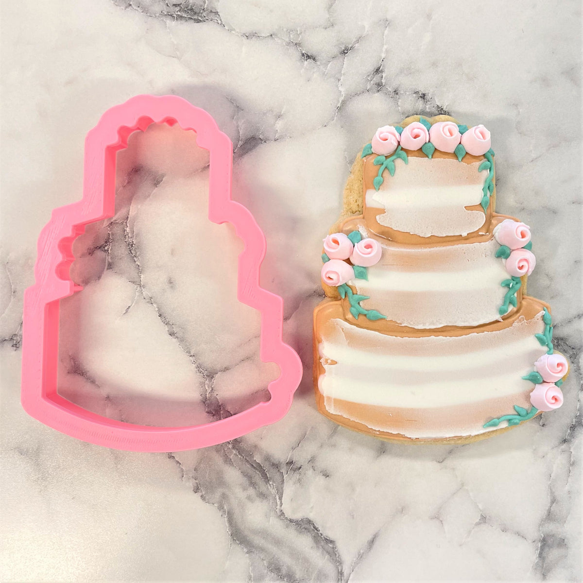 Pink silicone rustic wedding cake cookie cutter next to decorated sugar cookie replica for wedding treats
