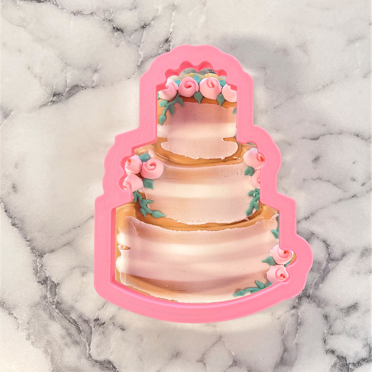 Pink silicone rustic wedding cake cookie cutter shaped like a three-tiered cake with pink and gold rose details