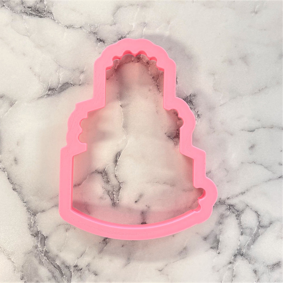 Pink silicone cookie cutter shaped like a tiered wedding cake for rustic wedding cake themed cookies