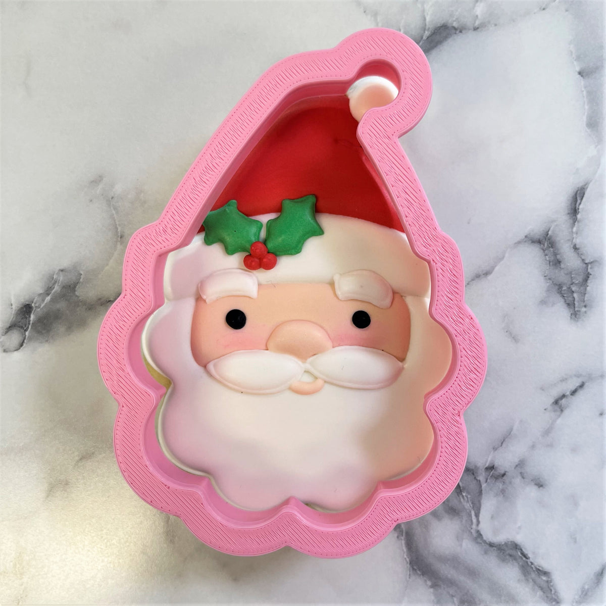 Pink silicone classic santa cookie cutter with red hat green holly and white beard details for baking