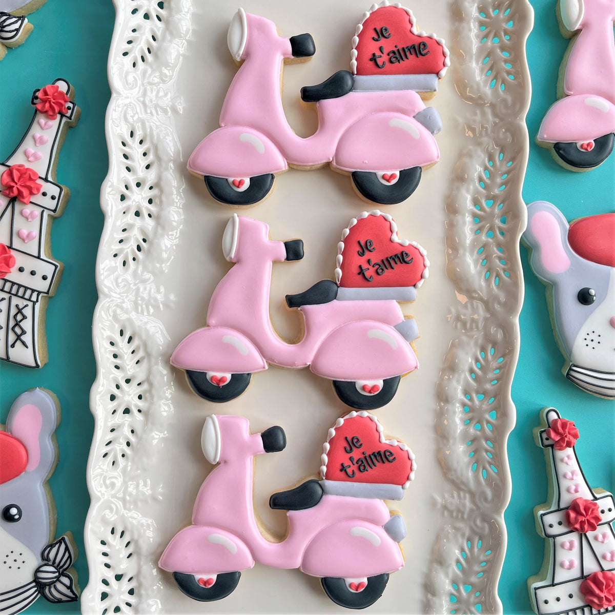 Pink scooter-shaped cookies with black wheels and red heart toppers reading je taime for paris valentine’s cookie class recording