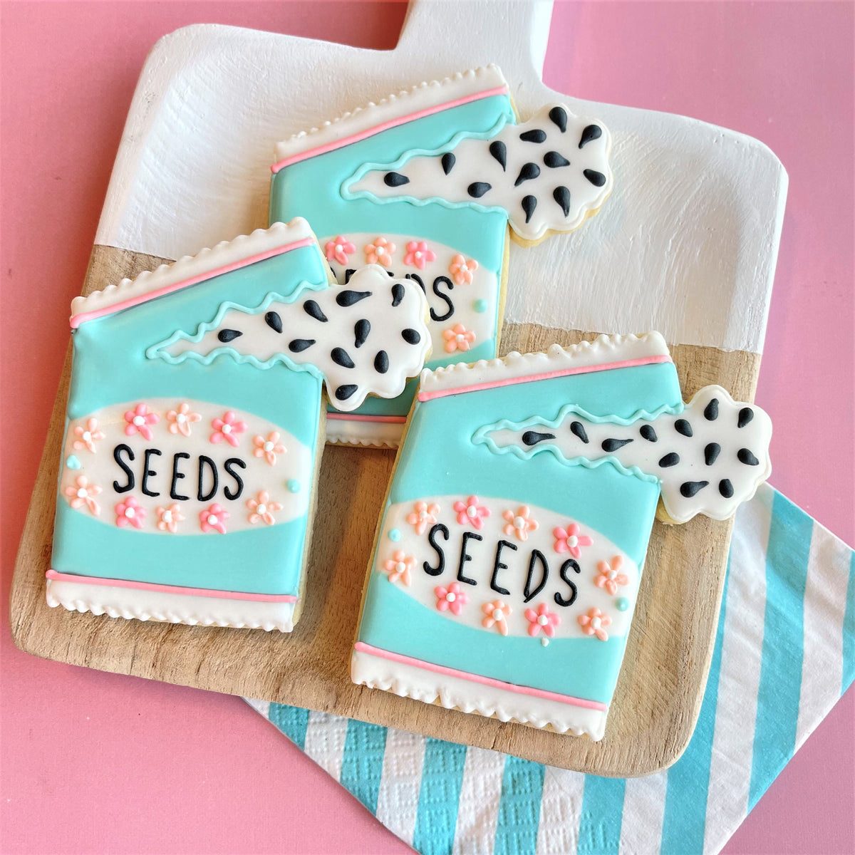 Pastel blue and white gardening mothers day sugar cookies shaped like seed packets with pink florals and black seeds