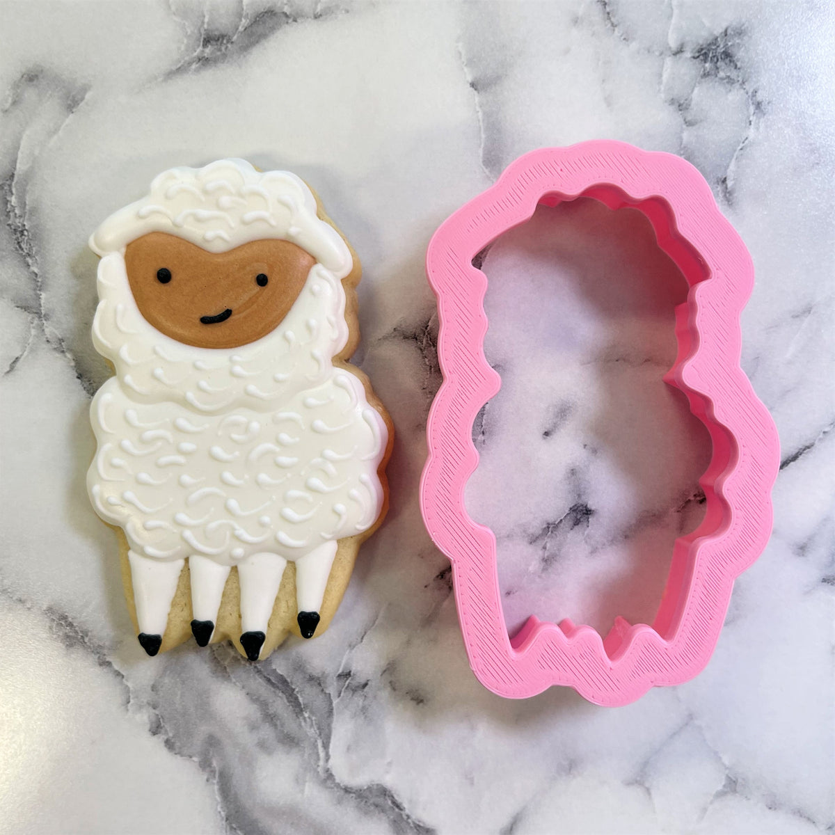 A pink silicone sheep cookie cutter with scalloped edge beside a decorated smiling lamb sugar cookie