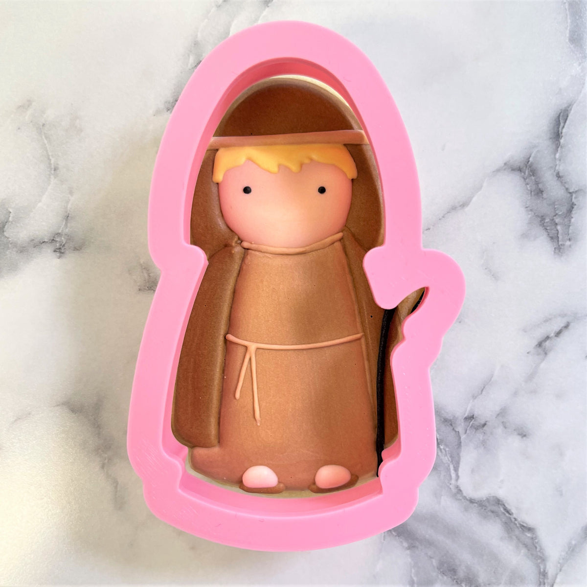 Pink silicone shepherd cookie cutter shaped like a cartoonish franciscan friar with blonde hair and brown robe