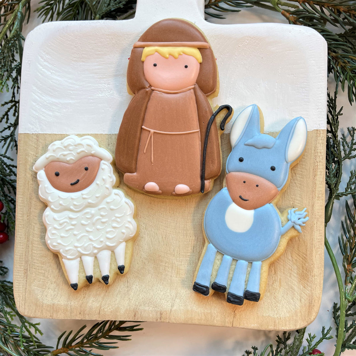 Three intricately decorated sugar cookies shaped like a franciscan friar sheep and donkey made with little donkey cookie cutter