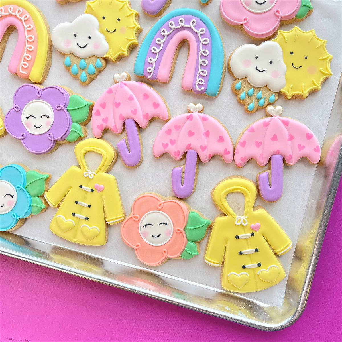 Pastel-colored sugar cookies shaped like rain clouds suns umbrellas and yellow raincoats with smiling faces from spring showers to flowers cookie decorating class recording