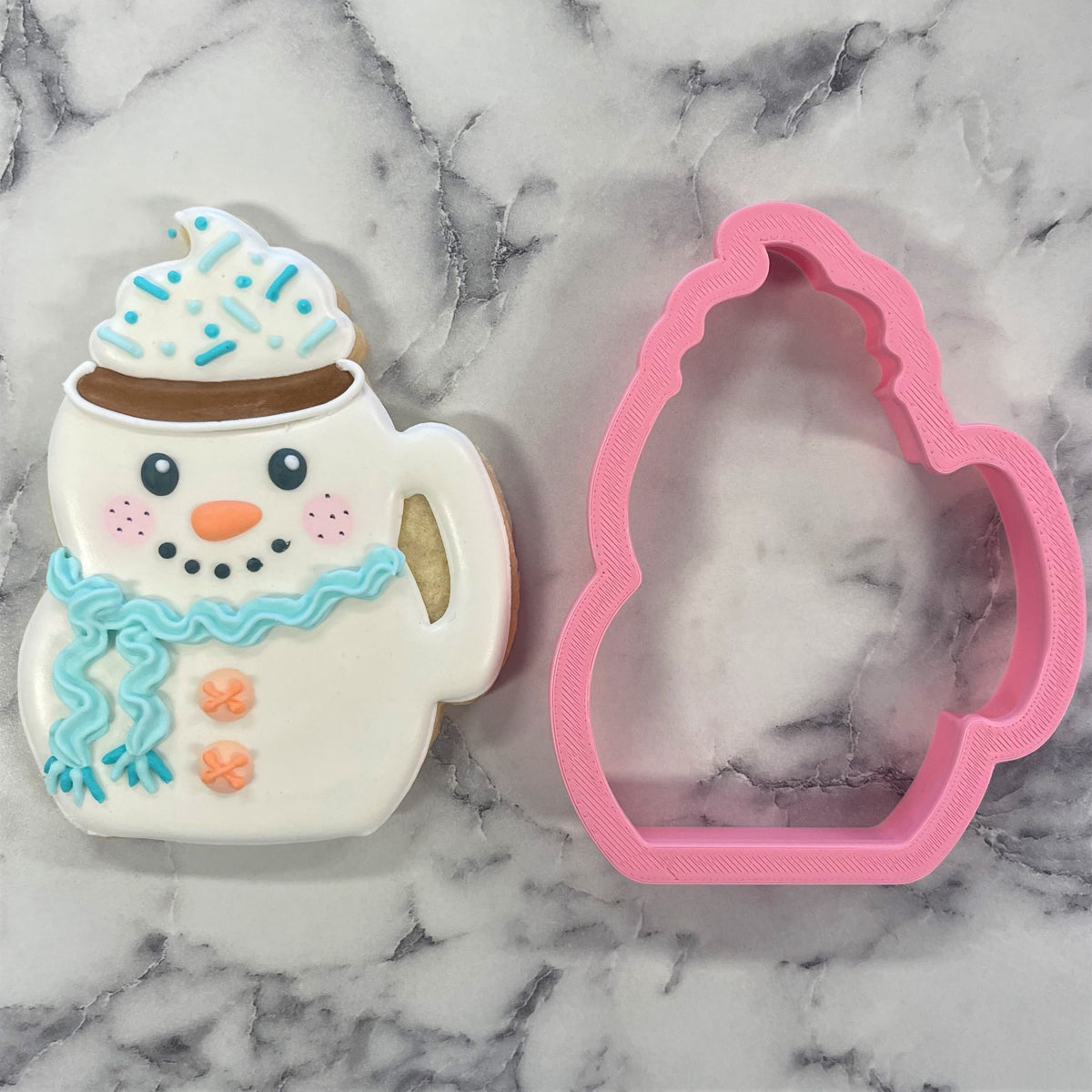 A white snowman-shaped cookie in a mug decorated with blue icing scarf and sprinkles for snowman mug flour box club