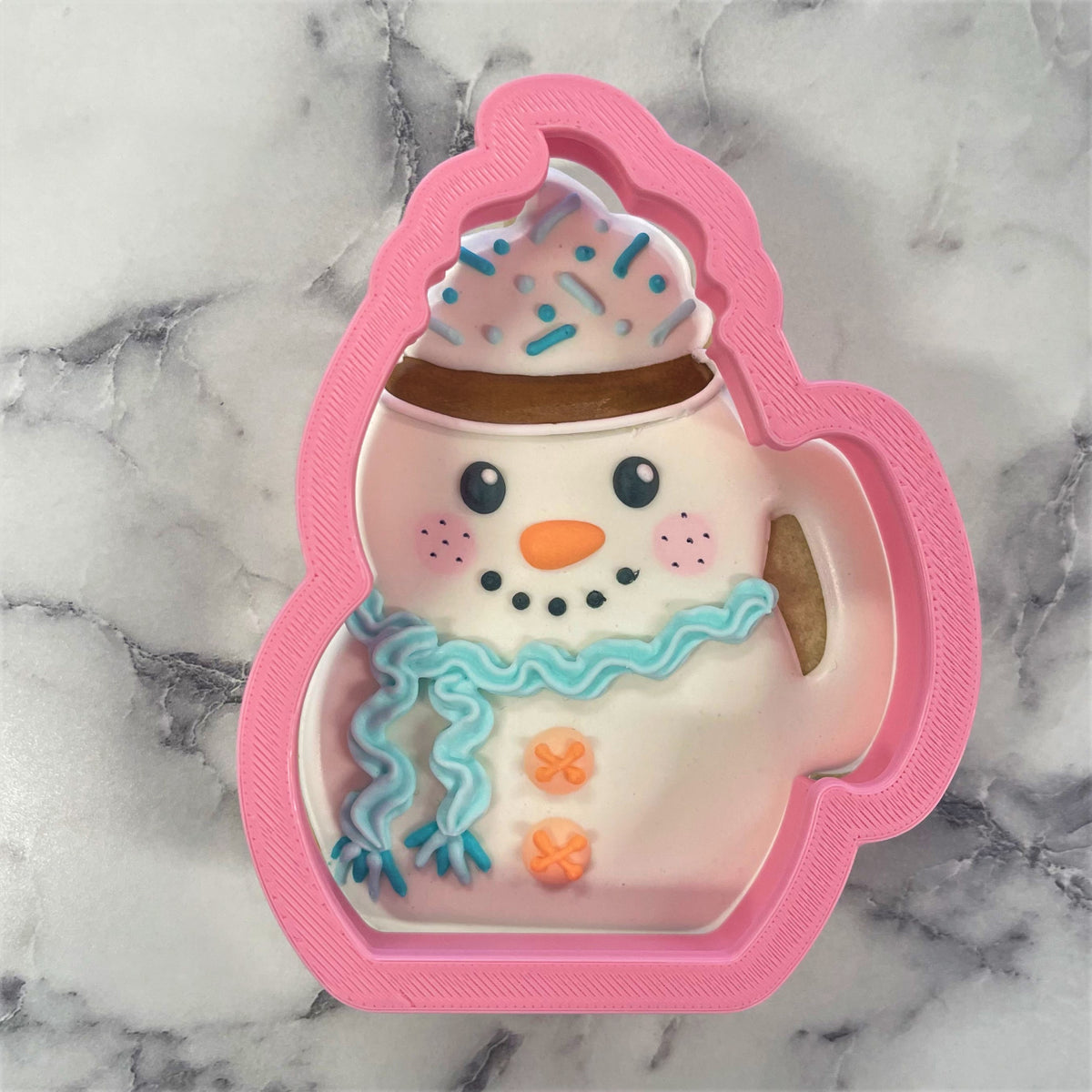 Pink plastic snowman-shaped cookie cutter in a mug with blue sprinkles and orange buttons for flour box club use